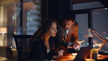 Fazla mesai başlatanlar akşam çalışma alanında strateji tartışıyorlar. Birlikte dizüstü bilgisayarı yakından izliyorlar. Profesyonel yöneticiler gece proje planlıyorlar. İki iş arkadaşı iş birliği yapıyor. 