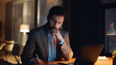 Ciddi bir iş adamı, karanlık bir dairede bilgisayar yazma notları karıştırıyor. Odaklanmış sakallı adam dizüstü bilgisayara bakıyor evde e-posta atıyor. Gece evinde çok çalışan yakışıklı CEO klavye çalıyor. 