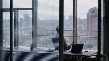 Rahatlamış müdür şehir manzaralı işyerinde espresso fincanının tadını çıkarıyor. Modern ofis içinde çalışan ciddi sakallı bir adam. Sakin zengin iş adamı görünümlü dizüstü bilgisayar masada tek başına oturuyor.