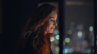 Lambanın ışığı altında fazla mesai yapan mutlu bir çalışan. Gülümseyen iş kadını, gece ofis alanında dizüstü bilgisayardan e-posta okuyor. Çalışkan kadın, gece geç saatlerde kapalı alanda proje geliştiriyor.