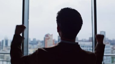 Anlaşmayı kutlayan mutlu girişimci silueti çağdaş ofis koridorunun arka penceresine el kaldırıyor. Pozitif yönetici cam ayırıcı ile heyecan gösteriyor. Memnun iş adamı başarının tadını çıkarıyor