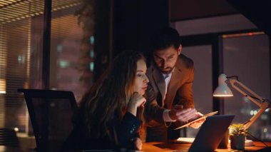 Genç girişimciler karanlık ofiste gece vardiyası sırasında hedeflerini analiz ediyor ve ekranı yakından izliyorlar. Yaratıcı stüdyoda mesai saatleri dışında takım çalışması planlama operasyonları düzenleyen odaklanmış iş arkadaşları