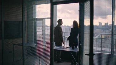 Siluet meslektaşları panorama penceresinden konuşuyor. Rahatlamış şirket yöneticileri, şehir manzarasını düşünerek birlikte çözüm arıyorlar. Şık iş adamı şehir manzarasını lüks işyerine yöneltiyor
