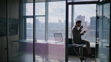 Zengin şirket çalışanı cep telefonu sosyal ağları okuyor panoramik vitrin ofisinde içecek masası içiyor. Yönetici sohbeti. Akıllı telefon. Kahveyle dinleniyor. Girişimci sakin bir mola veriyor 