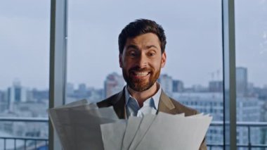 Panorama ofis portresinde heyecan hisseden bir yönetici. Duygusal iş adamı kağıtları fırlatıyor ve iş başarısını kutluyor. Çok memnun olan menajer tek başına sevinçle el kol hareketi yaparak anlaşmayı kazanıyor.