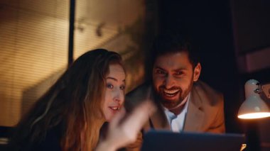 İki yönetici, akşam kurumsal iş yerinde dizüstü bilgisayar ekranında başarıya seviniyor. Heyecanlı meslektaşlarım duygusal tepki göstererek harika haberler okuyorlar. Coşkulu iş arkadaşları iş başarısının tadını çıkarıyorlar. 