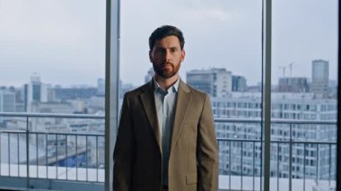 Zengin işyeri sahibi panoramik ofis girişinde kameraya bakıyor. Başarılı bir iş adamı poz verirken gülümsüyor. Zarif takım elbiseli pozitif patron şehir manzarasına olan güvenini ifade ediyor. 
