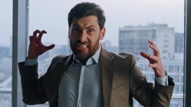 Öfkeli yönetici büyük pencerelerde ofis portresi gösteriyor. Kızgın patron kameraya bakıp el hareketi yapıyor. Stresli duygusal lider, şehir merkezindeki iş yerinde gerginliğini dile getiriyor.