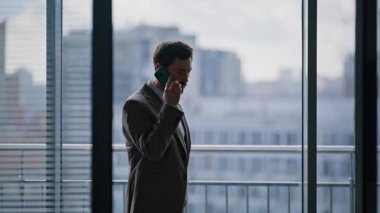 CEO 'nun telefon edip ofis penceresinin yakınına gelmesinden endişe ediyorum. Kendine güvenen sakallı yönetici stresli telefonda ciddi bir konuşma yapar. Sinirli iş adamı akıllı telefon konuşmalarıyla meşgul 
