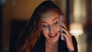 Akşamları çalışan bir iş kadını ofis masasında otururken akıllı telefondan konuşuyor. Çekici bayan yönetici cep telefonunu arıyor. Modern iş yerinde çalışıyor. Geç kalmış kadın yönetmen telefon kullanıyor. 