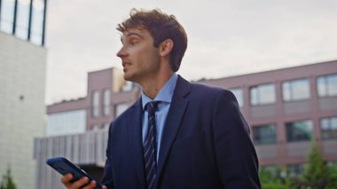Başarılı patron akıllı telefon tutuyor. Şehir içi iş yerlerini kapatıyor. Gülümseyen işadamı şehir caddesinde cep telefonuna bakıyor. Profesyonel yönetici şehir merkezinde dolaşan mesajları okuyor..