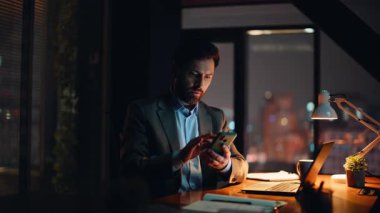 Koyu renk daire kapanışında cep telefonu uyarılarını kontrol eden serbest çalışan bir adam. Ciddi sakallı iş adamı akıllı telefon mesajı okuyor ve gece ofisinde notlar yazıyor. Geç saatte yönetici yalnız çalışıyor.