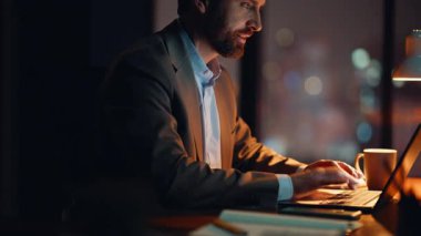 Karanlık işyerinde ışık altında fazla mesai yapan gülümseyen bir çalışan. Gece ofis alanında dizüstü bilgisayara mesaj atan mutlu iş adamı. Çalışkan adam gece geç saatlerde kapalı alanda proje geliştiriyor.