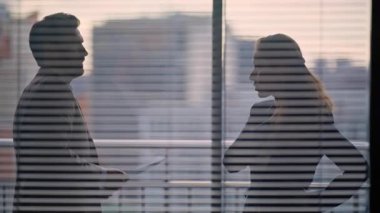 Modern mimari ofisindeki siluet işadamları sohbet ediyorlar. Bilinmeyen ortaklar karanlık panoramik pencerelerde konuşuyorlar. Meslektaşına kontrat belgelerini gösteren tanınmamış bir adam