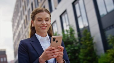 Gülümseyen yönetici şehir merkezinde akıllı telefon mesajı okuyordu. Kendine güvenen iş kadını dışarıda cep telefonuyla sohbet ediyor. Neşeli kadın şehir caddesinde cep telefonu ekranına bakıyor..