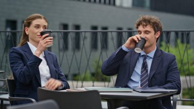 Rahat iş ortakları belediye binasının terasında birlikte kahve içiyorlar. Takım elbiseli iş arkadaşları dışarıda kahve içerek eğleniyorlar. Resmi olmayan toplantıda gülümseyen mutlu profesyoneller..