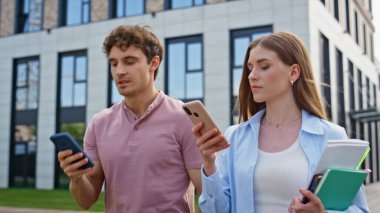 Modern binanın yakınındaki akıllı telefonları kullanan yürüyen yöneticiler. Odaklanmış kadın ve erkek, cep telefonlarını kontrol ediyor. Şehir caddesinde birbirlerine gülümsüyorlar. İki meslektaş işe giderken birden fazla iş yapıyor..