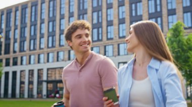 Gülümseyen kadın, modern ofis binasının yakınında kahveyle birlikte yürüyor. Şehir ortamında sabah sohbetinden zevk alan iki profesyonel. Mutlu arkadaşlar güneşli caddede geziniyor.