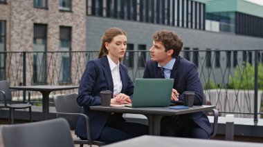 Profesyonel erkek kadın açık hava restoranı projesini tartışıyor. Modern kafeterya terasında laptopla iş birliği yapan odaklanmış iş arkadaşları. Kafedeki şirket toplantısında ciddi takım çalışması..