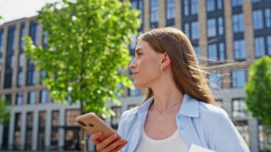 Modern binanın önünde yürüyen akıllı telefon görünümlü bir bayan. Yakın plan. Elinde cep telefonuyla dolaşan belgeleri tutan genç bir iş kadını. Saçları rüzgârlı şık bir kadın telefon mesajı okuyor.