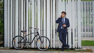 İş adamı dışarıda bisikletin yanında telefon görüşmesi yapıyor. Kahve molasında beyaz çitlerin önünde cep telefonuyla konuşan gülen bir müdür. Takım elbiseli kendine güvenen girişimci arkadaş canlısı mobil sohbetin tadını çıkarsın..