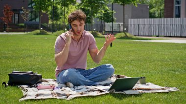 Neşeli serbest çalışan cep telefonunu arıyor. Yeşil çimlerde dizüstü bilgisayarla oturuyor. Gülümseyen adam akıllı telefondan konuşuyor güneşli park doğasının tadını çıkarıyor. Pozitif öğrenci cep telefonu konuşmasına ara veriyor..