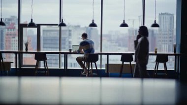 Şehir manzaralı ortak çalışma salonunda dizüstü bilgisayar yazan proje yöneticisi. Odaklanmış çalışanlar panoramik iç mekandaki kasvetli siluet mesajlarına bakıyor. Girişimci, bilgisayarla açık çalışma alanında oturuyor