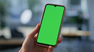 Freelancer cep telefonunu izliyor modern iş yerinde yakın çekim yapıyor. Kimliği belirsiz bir kadın elinde yeşil ekran akıllı telefon mesajı tutuyor. İş kadını Chroma Key cep telefonunda bankacılık uygulamasına göz atıyor
