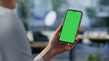 Şirket işyerindeki yeşil ekran cep telefonlu kadın el ele tutuşma mesajı. Bilinmeyen iş kadını yeşil ekran cep telefonunda bankacılık uygulamasına göz atıyor. Ofisteki kadın video içeriğini izliyor.