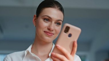 Ofiste cep telefonuna mesaj atan mutlu esmer portre. Modern işyerindeki akıllı telefon mesajlarına cevap veren güzel bir genç kadın. Gülümseyen kadın apartmanda online iletişimden hoşlanıyor..