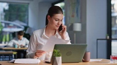 Yönetici arıyor. Dizüstü bilgisayar arıyor. Ofis açık alanda yakın plan çekimde. İş yerinde akıllı telefondan konuşan neşeli bir iş kadını. Zarif kadın CEO cep telefonu konuşmasında rapor sunuyor.