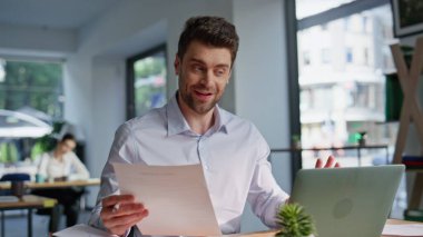 Gülümseyen İK yöneticisi internet röportajında konuşuyor. İş yerindeki internet kameralarına bakıyor. Dost canlısı iş adamı videosu elinde kağıtlarla arıyor. Profesyonel danışman ofisinde sanal müzakere yapıyor.