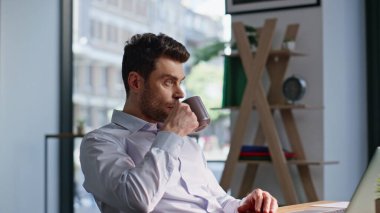 Müdür modern ofisin açık mekanında kahve molası veriyor. Rahat iş adamı sıcak çayını yudumluyor ve iş yerinde oturuyor. Resmi gömlekli sakallı şirket çalışanı elinde içecek bardağıyla dinleniyor..