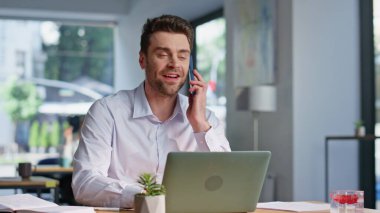 Modern çalışma alanlarında arkadaş canlısı serbest çalışan akıllı telefonlar. Gülümseyen işadamı iş planlarını telefonla tartışıyor. Pozitif yönetici cep telefonuyla ofis bilgisayarından sipariş veriyor..