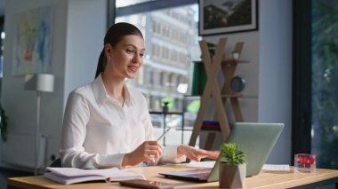 Çevrimiçi konferansta konuşan danışman modern ofiste evrakları yakın çekimde tutuyor. Gülümseyen iş kadını iş anlaşmasını video görüşmesiyle tartışıyor. Laptop webcam 'e belge gösteren pozitif kadın yönetici.