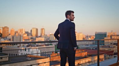 Gülümseyen CEO terasta dinleniyor ve gün batımı manzarası seyrediyor. Balkon korkuluklarında duran şık takım elbiseli mutlu bir işadamı. Başarılı bir işletme sahibi akşam ışığında şehir arıyor..