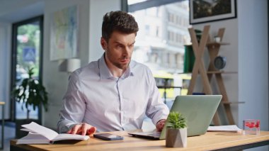 İş yerinde dizüstü bilgisayarı daktilo eden odaklanmış girişimci. Ciddi sakallı iş adamı internette araştırma yapıyor. Defterdeki verileri kontrol ediyor. Ofisteki bilgisayar açık alanda akıllı serbest programlama.