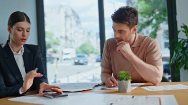 Ofis toplantısında vergi belgelerini tartışan profesyoneller. İş kadını, güler yüzlü yatırımcı masasına proje karı hesaplıyor. İş ortakları mali bütçeyi tartışıyor.