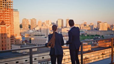 Ofisteki iş arkadaşları gün batımı çatısı manzarasına bakıyor. Profesyonel iş kadını akşam ufkunda ayakta duran işi tartışıyor. İki iş arkadaşı altın güneş ışığında dışarıda mola veriyor..