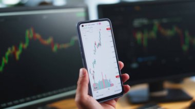 Borsacı elinde borsa çizelgeleriyle cep telefonu tutuyor. Tanımlanamayan tüccar cep telefonu ve bilgisayar çoklu monitörlerindeki döviz grafiklerini analiz ediyor. Finansal yatırım kavramı.