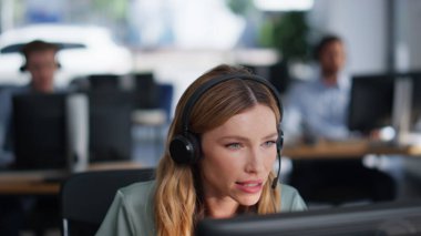 Yardımcı masa uzmanı kulaklıkla müşteriyle konuşuyor. Ofis kapanışında çalışıyor. İnternette danışmanlık yapan profesyonel bir kadın. Kulaklıklı çağrı merkezi operatörü istemciye tavsiyede bulundu.