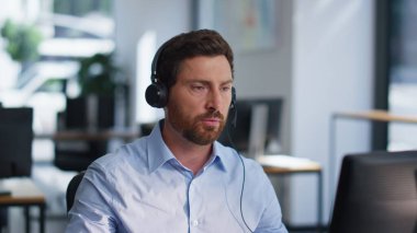 Çevrimiçi yönetici kulaklıkla konuşuyor. Ofiste açık alanda teknik müşteri desteği sağlıyor. Çağrı merkezinde çalışan ciddi bir adam. Hizmet masası uzmanı müşteriye iş yerinde yardım ediyor