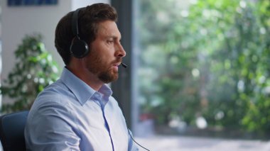 Klavye yazma teknisyeni müşteri sorunlarını uzaktan çözüyor. Kulaklık takan sakallı adam açık alanda teknik servis sağlıyor. Erkek danışman konuşan müşteri görünümlü bilgisayar