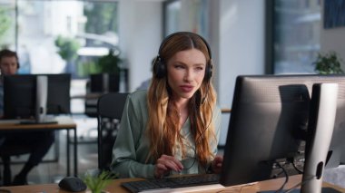 Ofisteki ortak çalışma alanındaki bilgisayar verilerine bakan bir danışman. Gülümseyen kadın yardım hattı operatörü müşteriyle konuşuyor. Profesyonel yönetici kulaklıkla danışmanlık yapıyor.