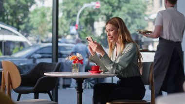 Kahve molasında restoranda dinlenen rahat bir kadın cep telefonu mesajı okuyor. Gülümseyen iş kadını kafede akıllı telefon ihbarı alıyor. Kapuçino ile kafeteryada oturan mutlu sarışın bayan..