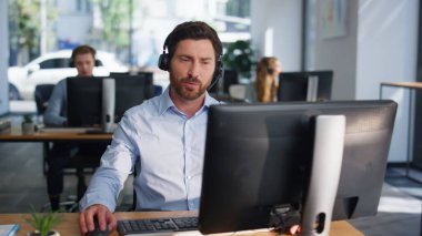 Müşteri hizmetleri danışmanı, müşterinin yakın çekim alanında kulaklıkla konuşmasına yardım ediyor. Ofisteki çağrı merkezinde teknik destek sağlayan sakallı adam. CRM pazarlama uzmanı şirket ürünü öneriyor.