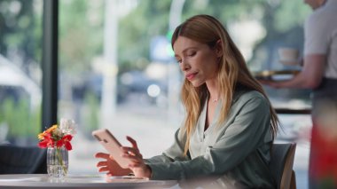 Restoran masasında oturan zarif bayan cep telefonunu kapatma süresini kontrol ediyor. Samimi kafeteryada kendine güvenen bir iş kadını bekliyor. Rahat bir kadın modern kafede tek başına rahatlıyor. Akıllı telefon gibi görünüyor..