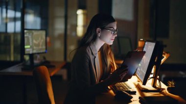 Gece yatırımcısı modern çalışma alanındaki dokunmatik ekran cihazını kullanarak verileri analiz ediyor. Mutlu kadın akşam saatlerinde ev ofisinde çalışmaya odaklanmış. Piyasa eğilimlerini araştıran finans tüccarı