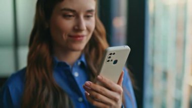 İş kadını elleri şirket işyerinde cep telefonu tutuyor. Gülümseyen iş kadını modern ofisteki akıllı telefondan mesaj atıyor. Mutlu kadın serbest çalışan içeride cep telefonu kullanarak internette sohbet ediyor.