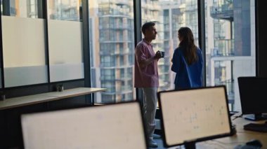 Ofis arkadaşları panoramik bina penceresinde kahveyi paylaşıyorlar. Rahatlamış iş arkadaşları şehir manzarasının tadını çıkarıyorlar birlikte aromatik içecekler içiyorlar. Zarif bir kadın iş yerinde dost canlısı bir adamla konuşuyor. 